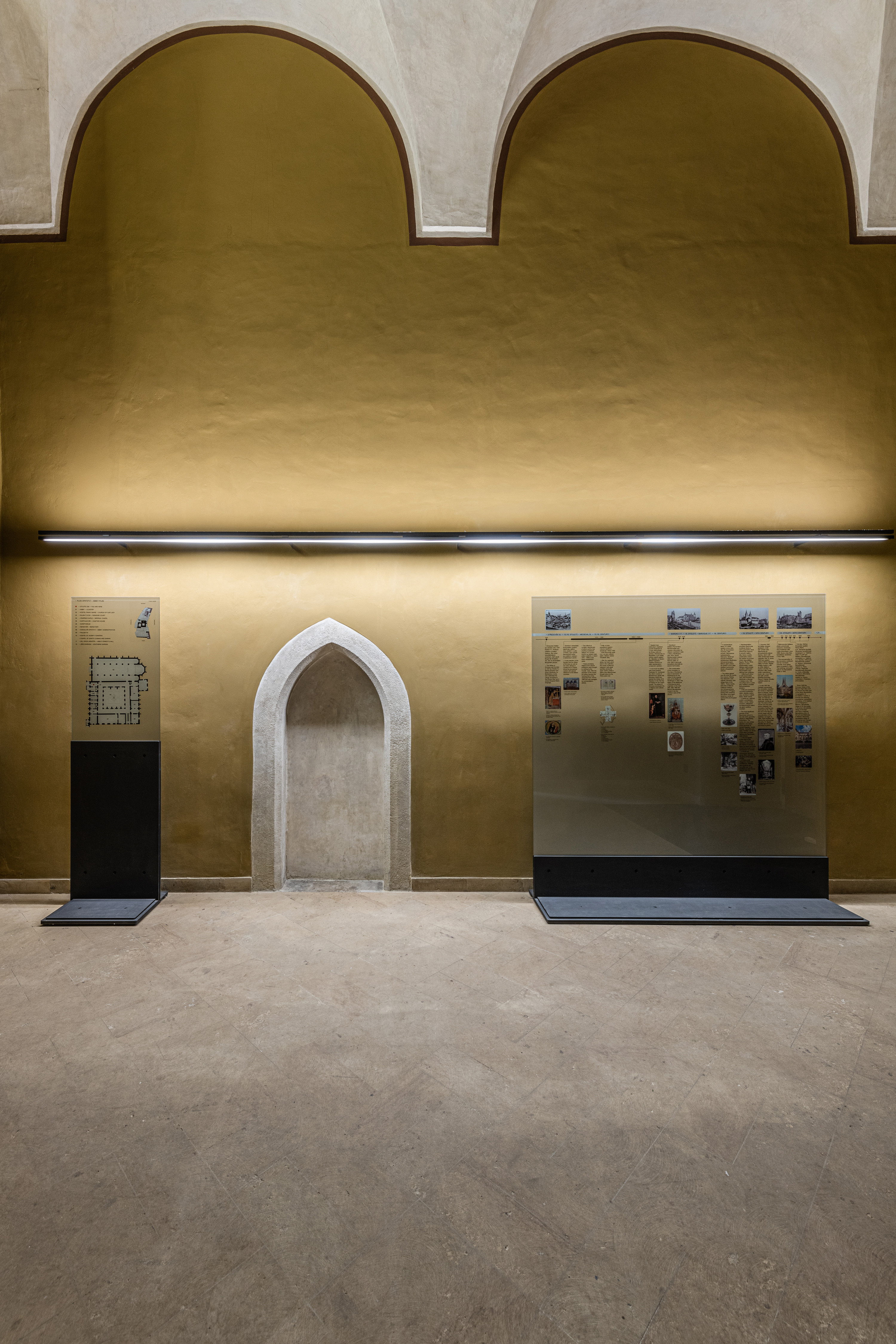 The exhibition wall in Emmaus Abbey has an illuminated arch and informational panels, using an understated design in line with the abbey's identity and modest navigation principles.