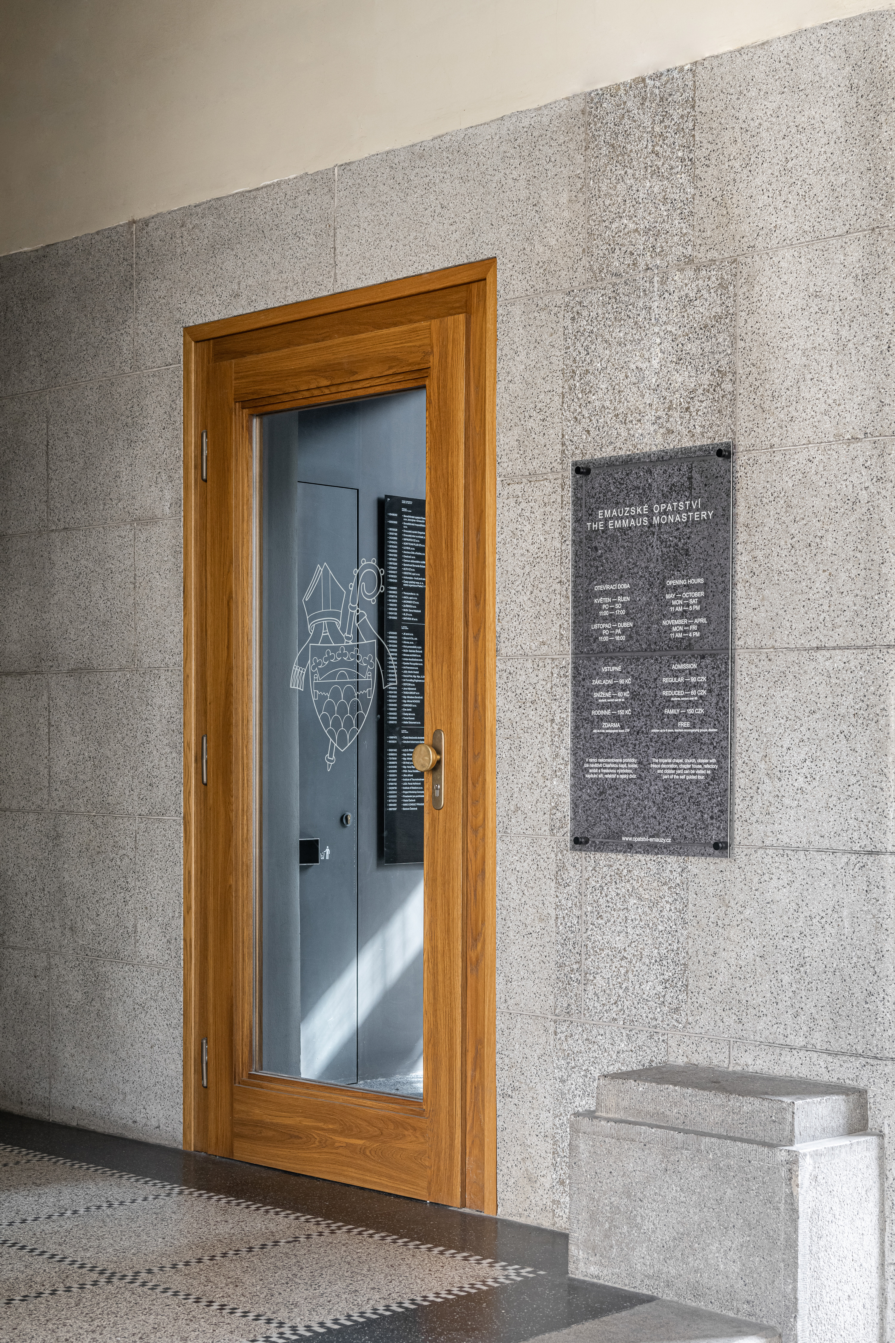 Wooden door with a glass panel at Emmaus Abbey, featuring modest navigation graphics and engraved Benedictine symbols, exemplifying the abbey's identity and adherence to 'Pray and work' in a humble design.