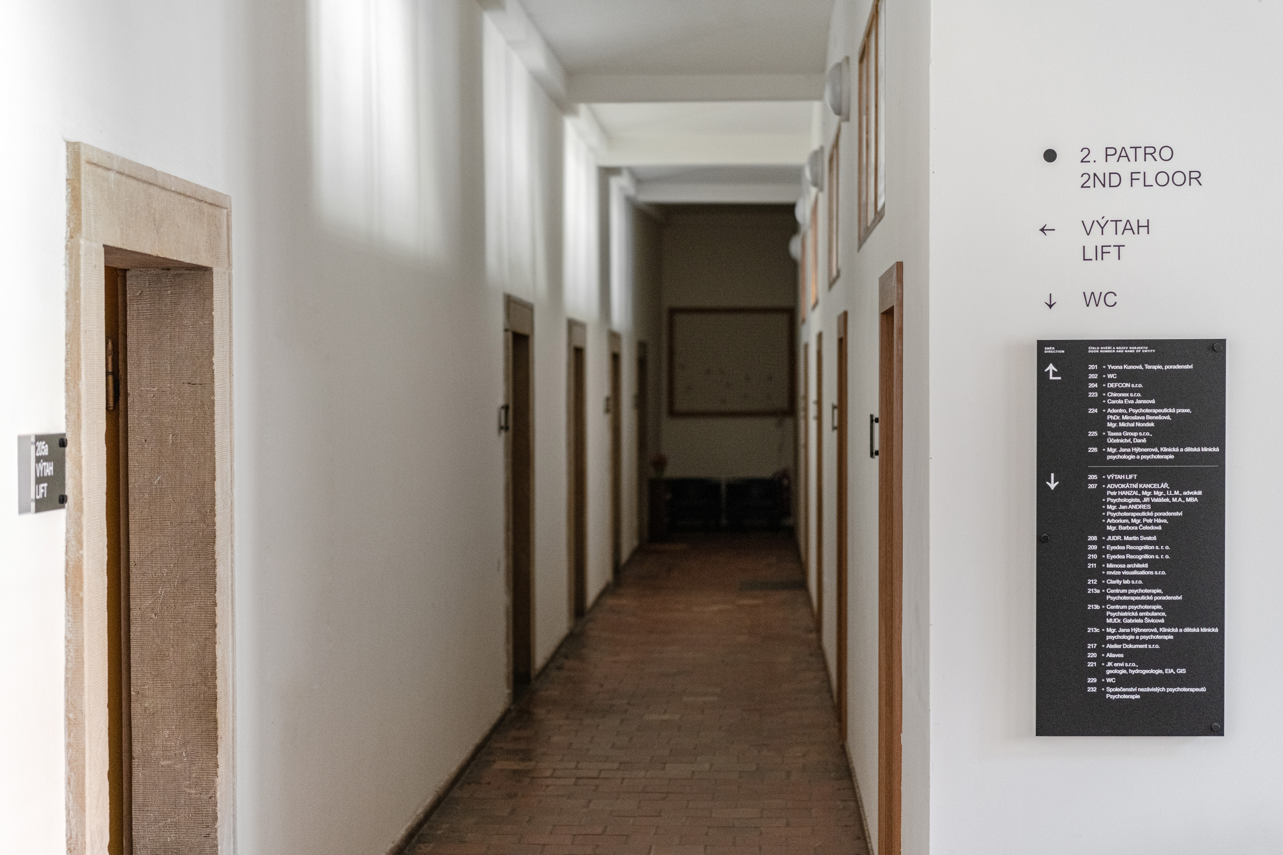 A simple, well-lit corridor in Emmaus Abbey with directional signage in Arial font facilitates navigation and aligns with the abbey's self-sustaining, modest identity.