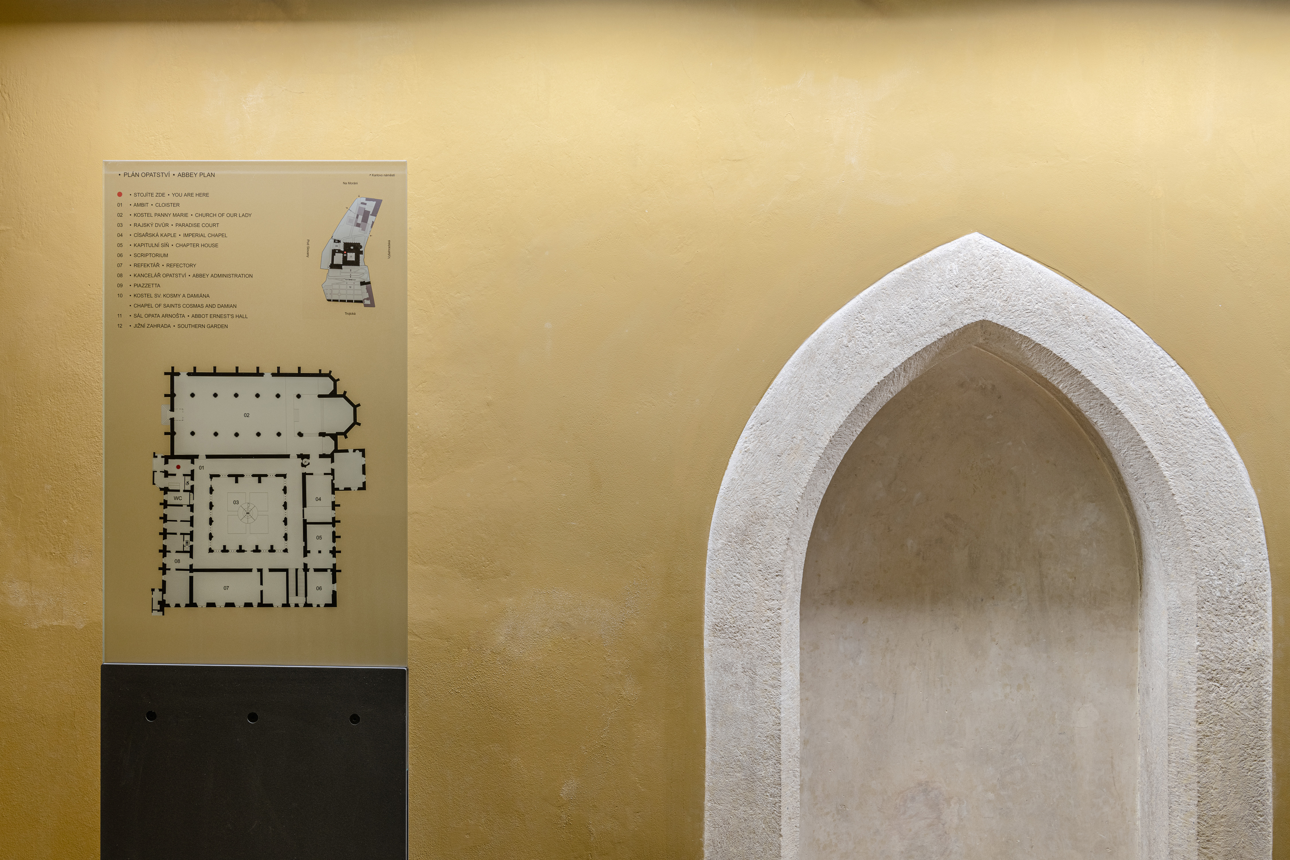 A detailed map and directory of Emmaus Abbey are on a wall, featuring Arial font in a minimalist layout, embodying the abbey's identity and practical self-maintenance navigation system.